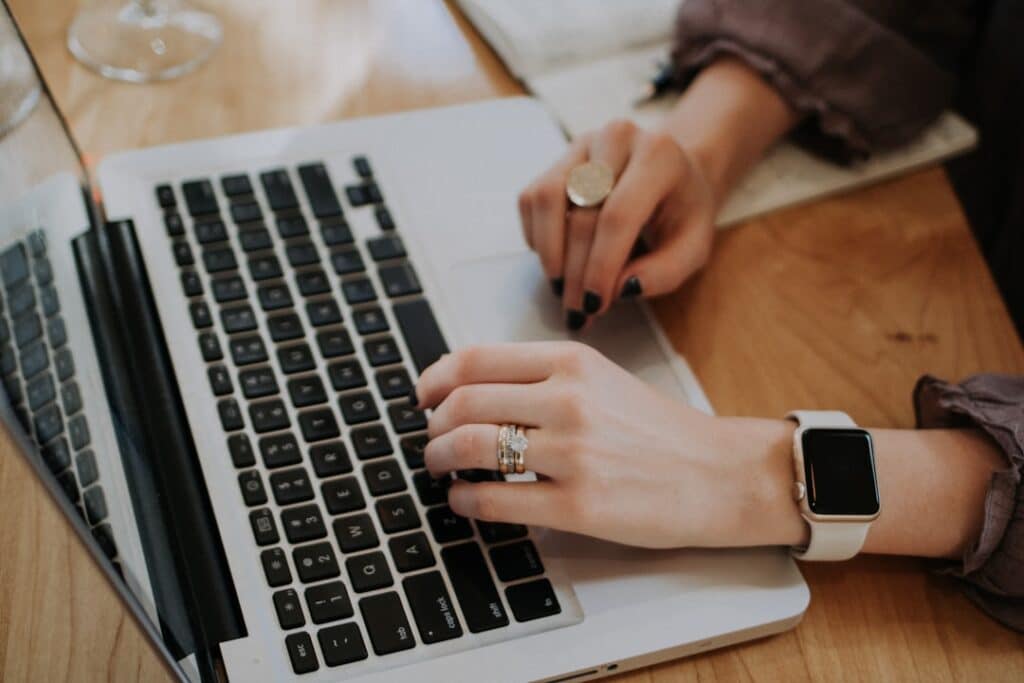 An individual typing on a laptop with a watch, engaged in research about AI management strategies.