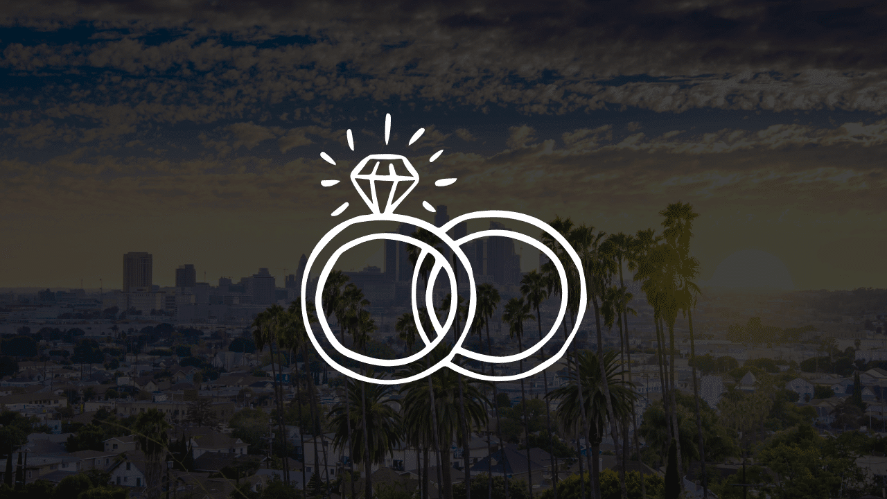 A white line art icon of intertwined wedding rings over a scenic sunset view of the Los Angeles skyline and palm trees, showcasing a beautiful Los Angeles wedding at Lucky Wedding Day Chapel.